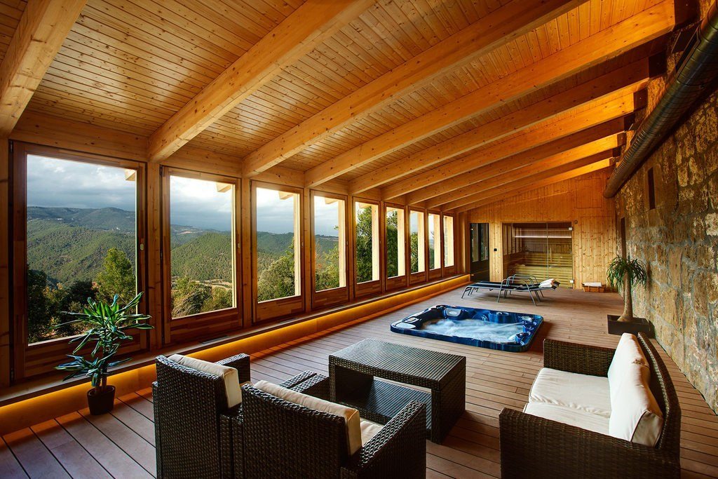 Timber-ceilinged garden room with wide windows, soft seating and a view over green hills